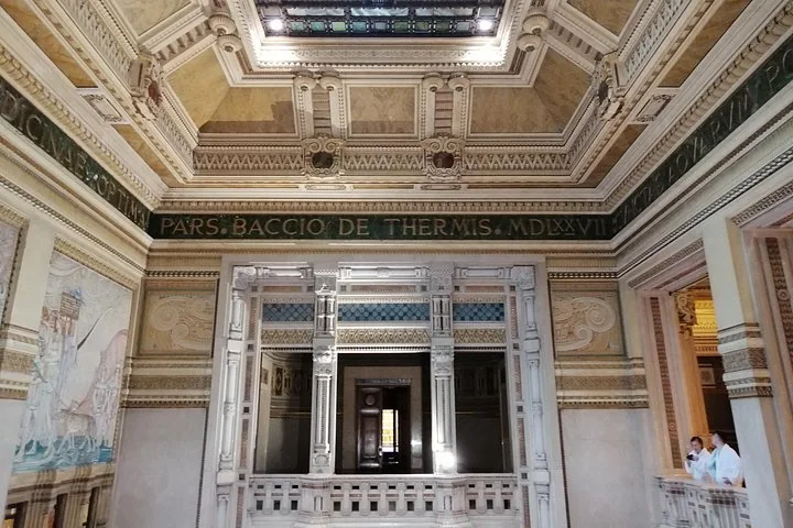 A frescoed hall with a coffered ceiling and a Latin inscription frieze above a marble balustrade
