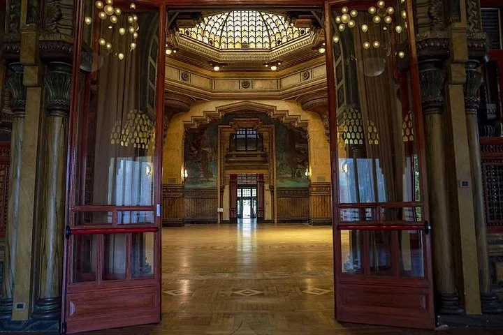 A grand hall with a stained-glass dome, painted walls and a parquet floor, seen through open red doors